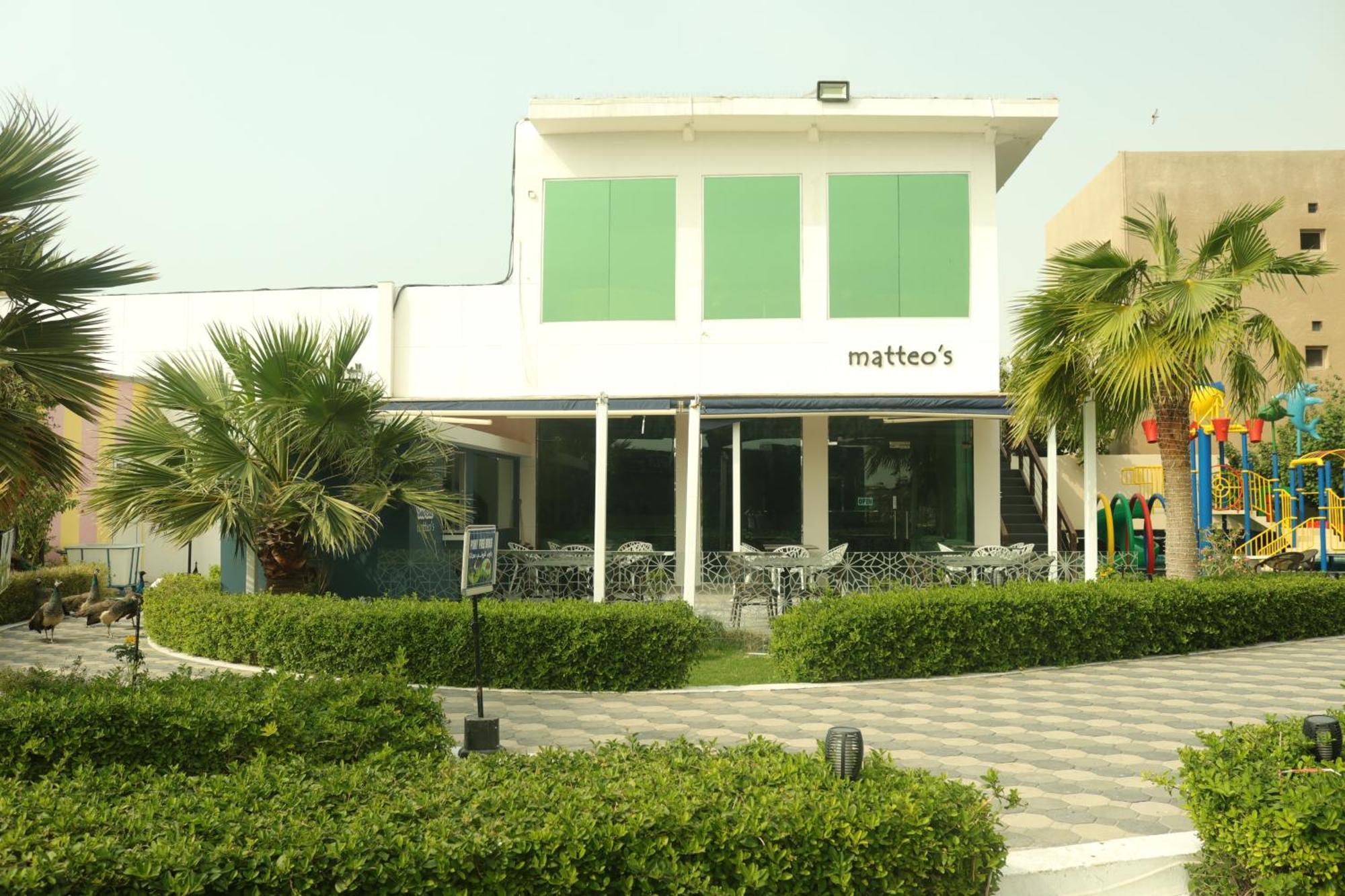 Lagoona Beach Luxury Resort And Spa Manama Eksteriør billede The photo shows a building with the name "matteo's" displayed prominently on the front. The structure features large windows and green shutters. There is a landscaped area in front with bushes and palm trees, along with a paved pathway leading up to 