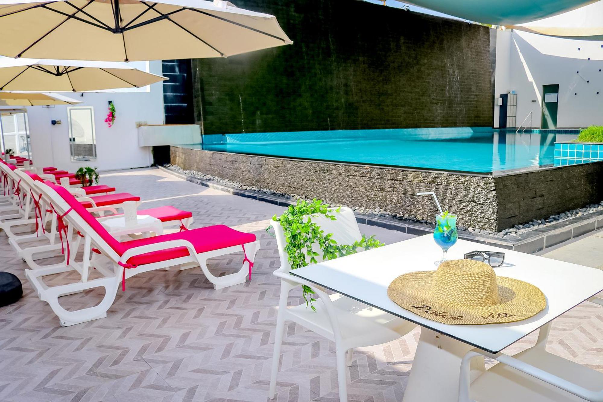Lagoona Beach Luxury Resort And Spa Manama Eksteriør billede The photo shows a sunny poolside area with bright red lounge chairs arranged neatly beside a swimming pool. There are large beige umbrellas providing shade. A small table is set up with a straw hat and a colorful drink, suggesting a relaxed, tropical