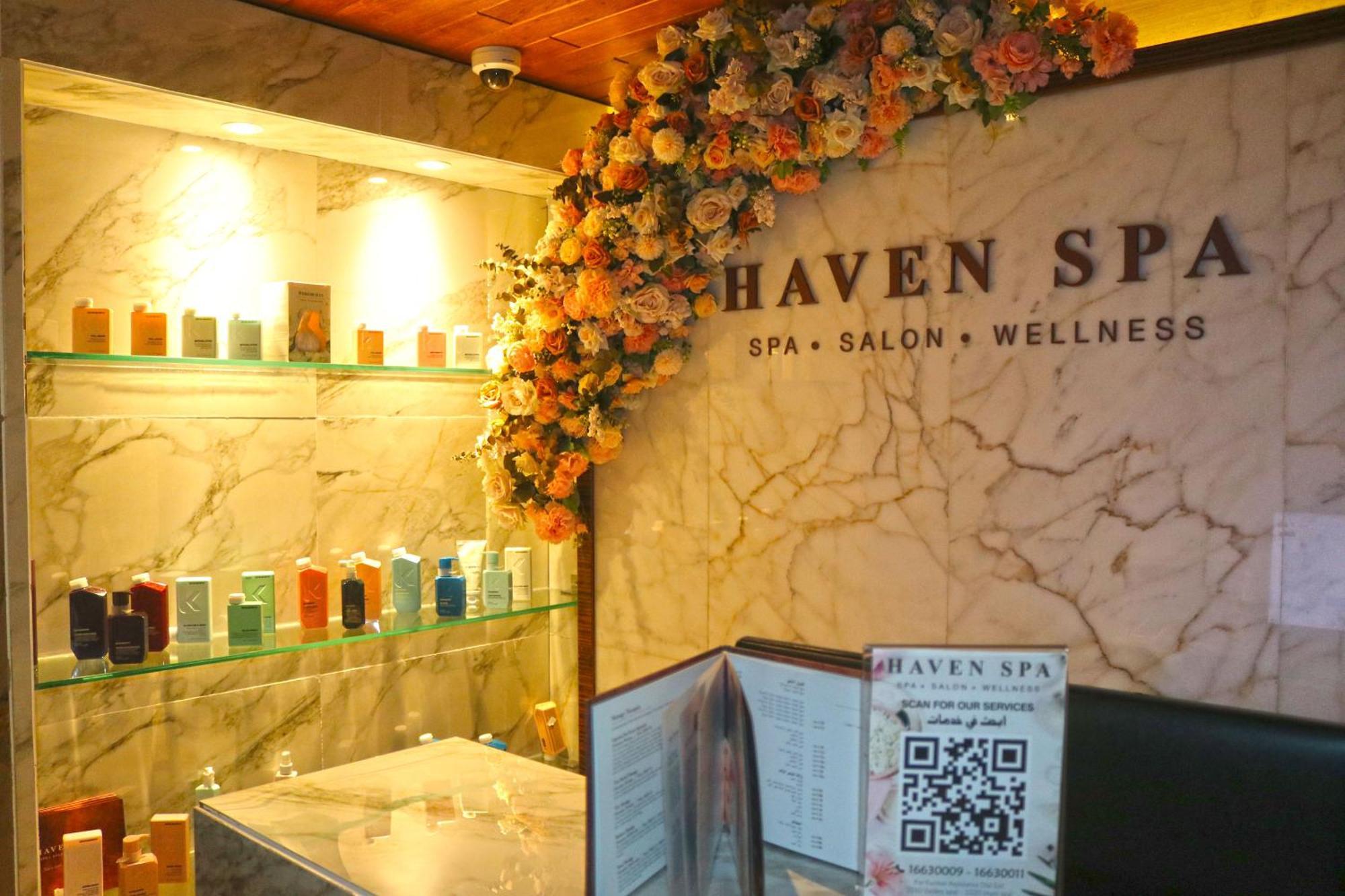 Lagoona Beach Luxury Resort And Spa Manama Eksteriør billede The photo shows the interior of a spa called "Haven Spa." The wall is decorated with beautiful artificial flowers, creating an inviting atmosphere. There are several shelves displaying various colorful bottles and products, likely for skincare or wel