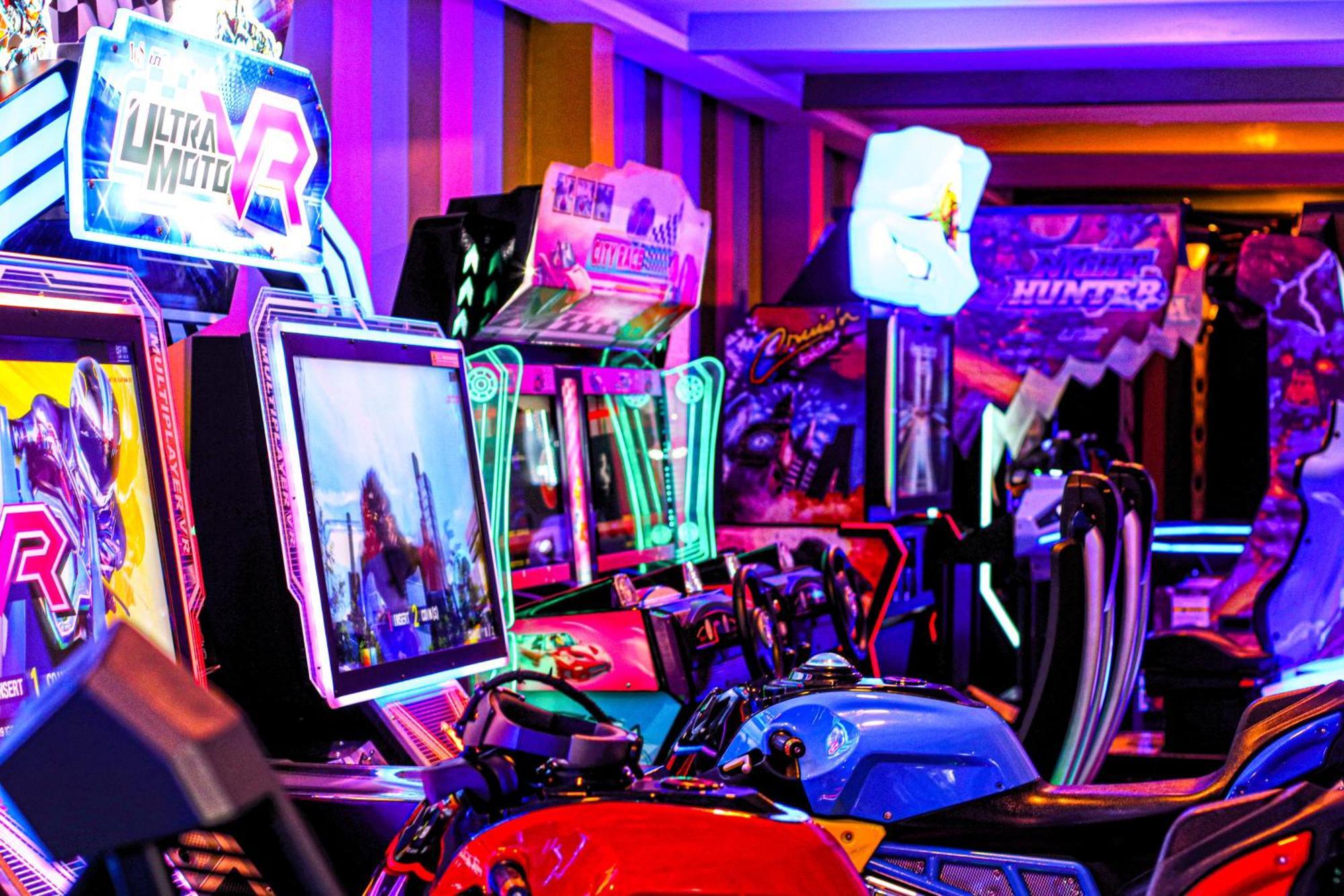 Lagoona Beach Luxury Resort And Spa Manama Eksteriør billede The photo shows a vibrant arcade scene featuring various arcade gaming machines. The machines are lined up, showcasing colorful screens and bright, neon lights, creating an energetic atmosphere. Some machines appear to be racing games, as indicated b