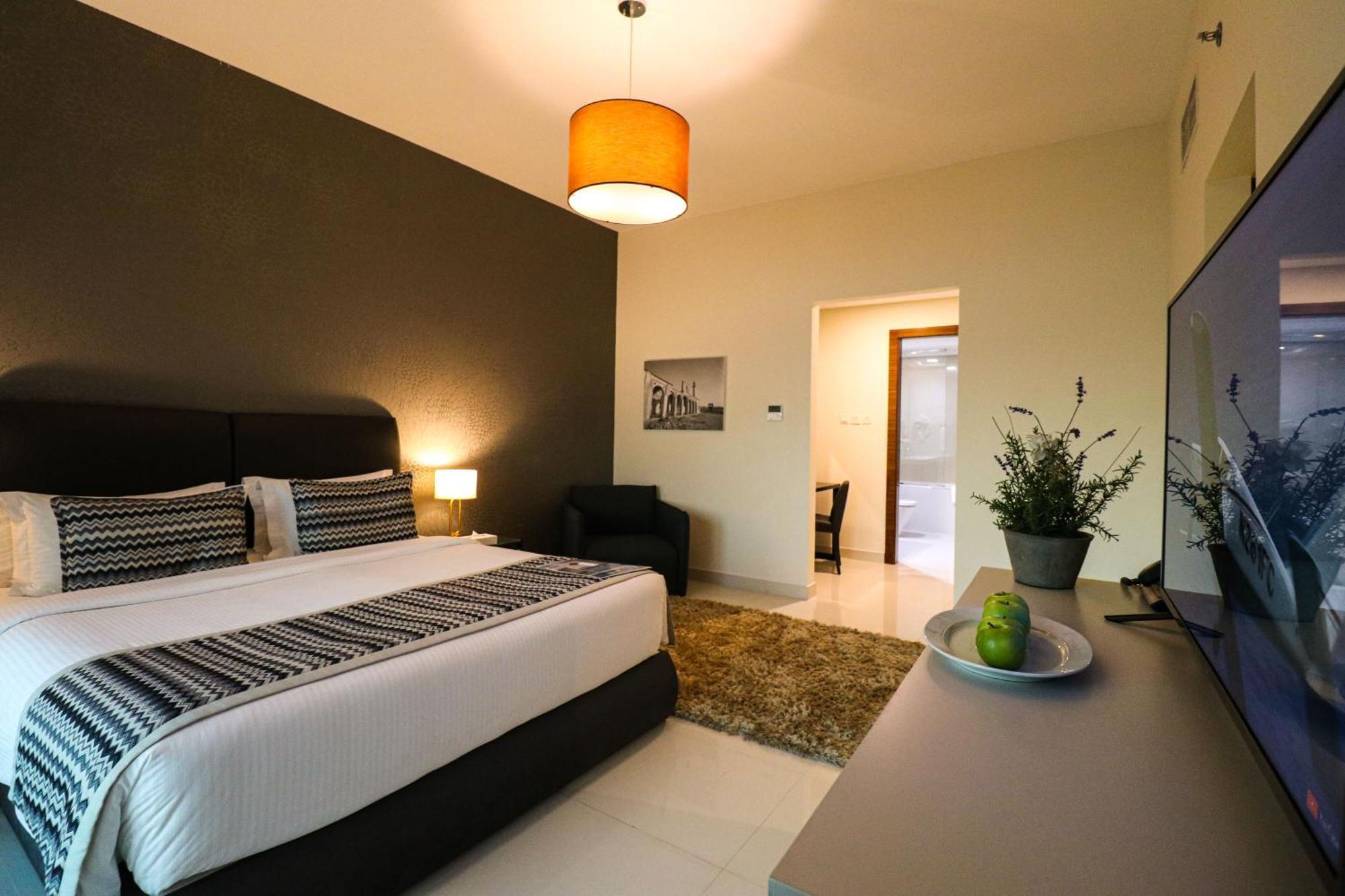 Lagoona Beach Luxury Resort And Spa Manama Eksteriør billede The photo shows a modern hotel room. It features a large bed with a neatly made white and dark-colored duvet. On either side of the bed, there are bedside tables with lamps. The wall behind the bed is painted in a dark color, creating a contrast with