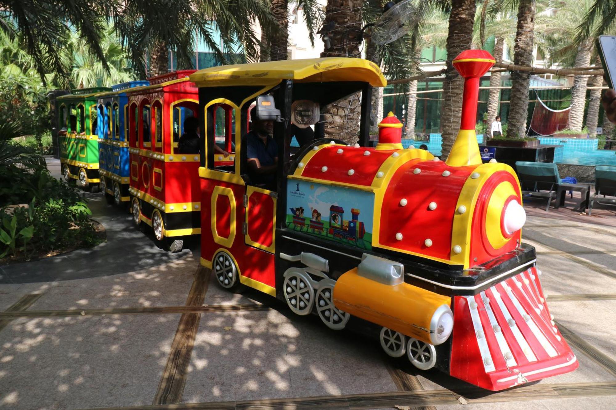 Lagoona Beach Luxury Resort And Spa Manama Eksteriør billede The photo shows a colorful miniature train. It features a vibrant design with bright red, yellow, and blue colors. The front of the train resembles a classic steam engine, complete with a prominent smokestack. The train is designed to resemble a fun 