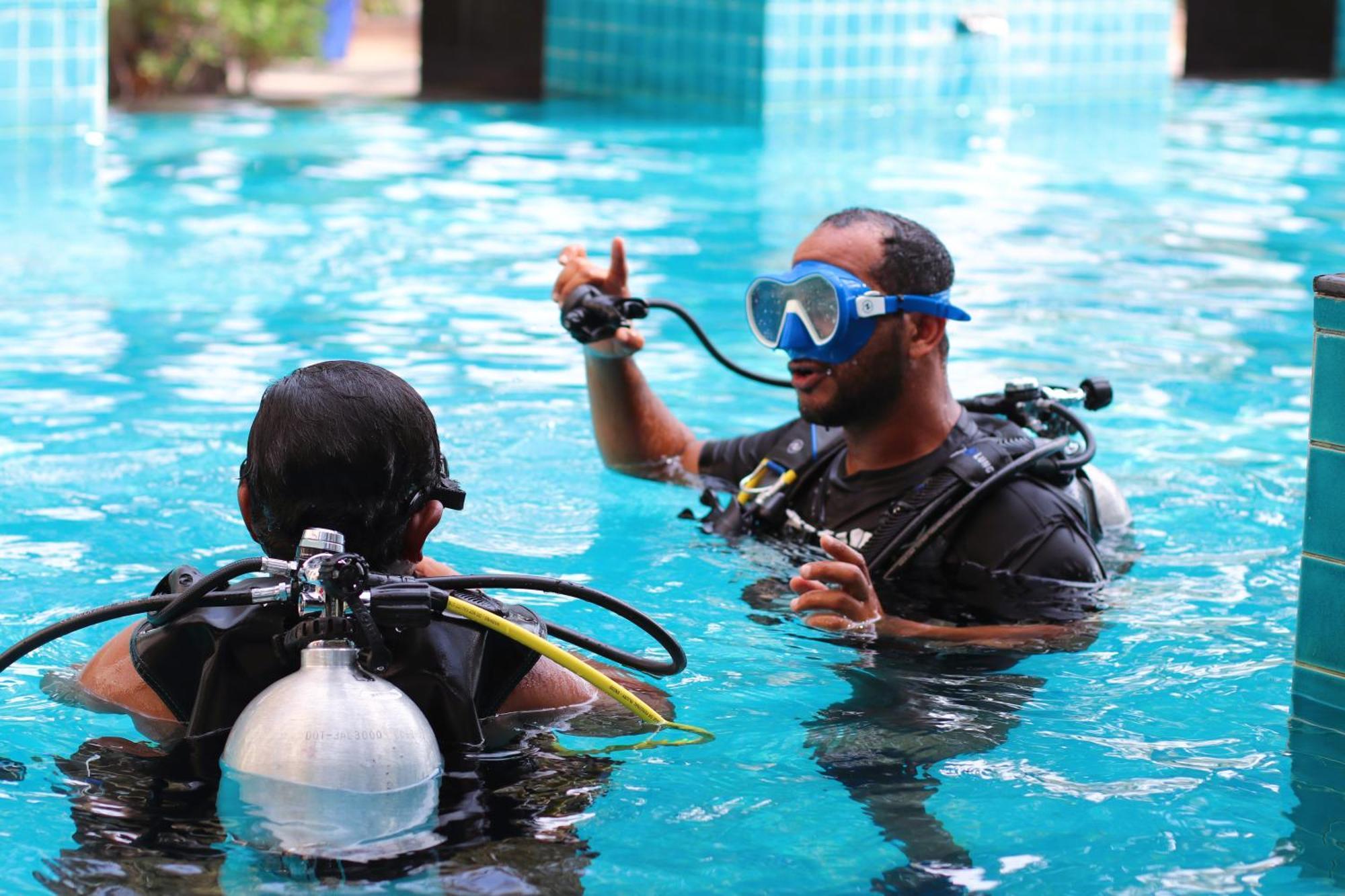 Lagoona Beach Luxury Resort And Spa Manama Eksteriør billede The photo shows two divers in a pool. One diver is wearing a scuba mask and is speaking to the other diver, who is also equipped with scuba gear. They appear to be engaged in a discussion, possibly related to diving instructions or safety. The water 