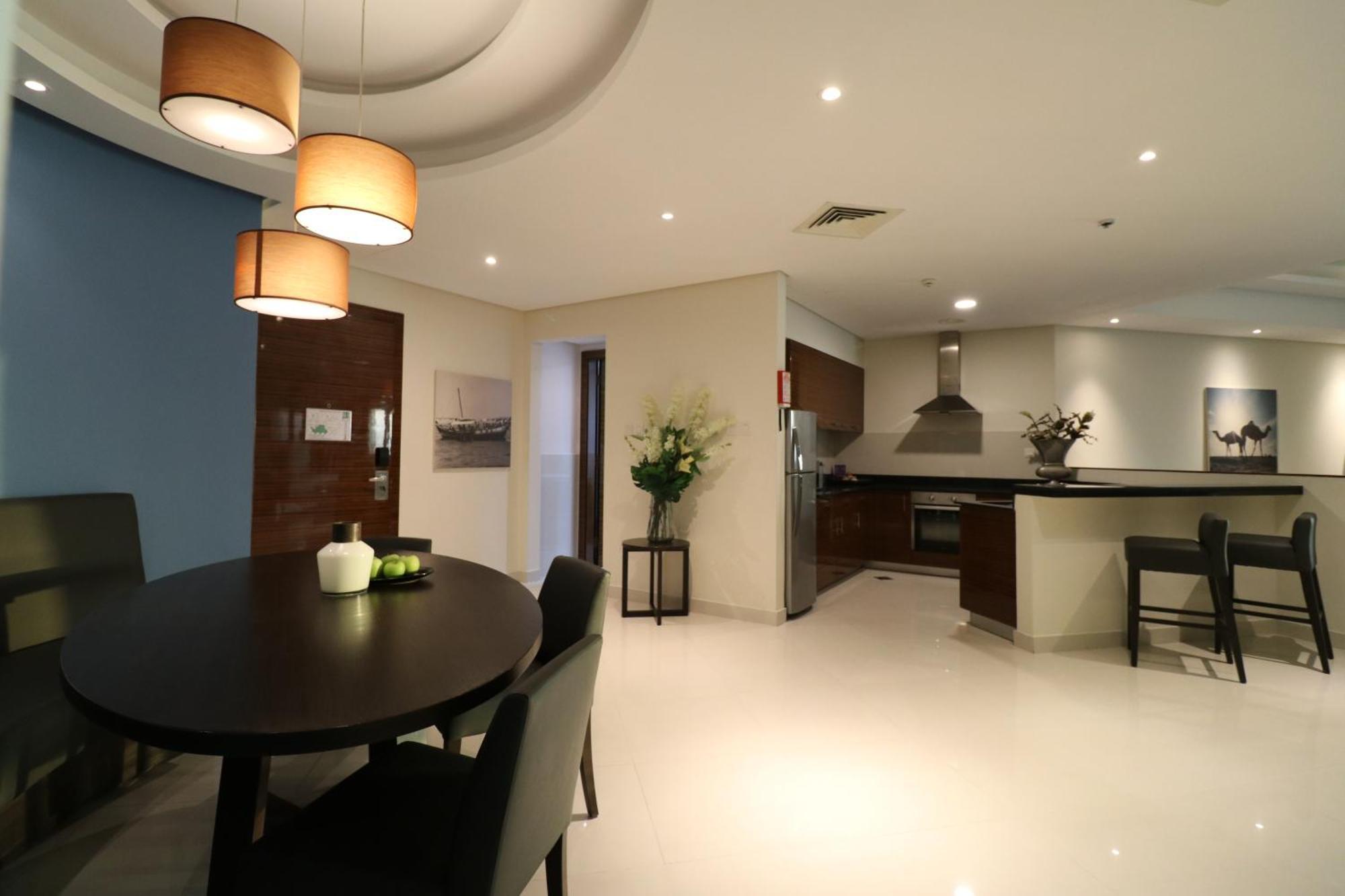 Lagoona Beach Luxury Resort And Spa Manama Eksteriør billede The photo shows a modern, open-concept dining and kitchen area. On the left, there is a round dining table with black chairs, accompanied by a few decorative elements like a small vase and some fruit. The walls have a combination of light and dark to