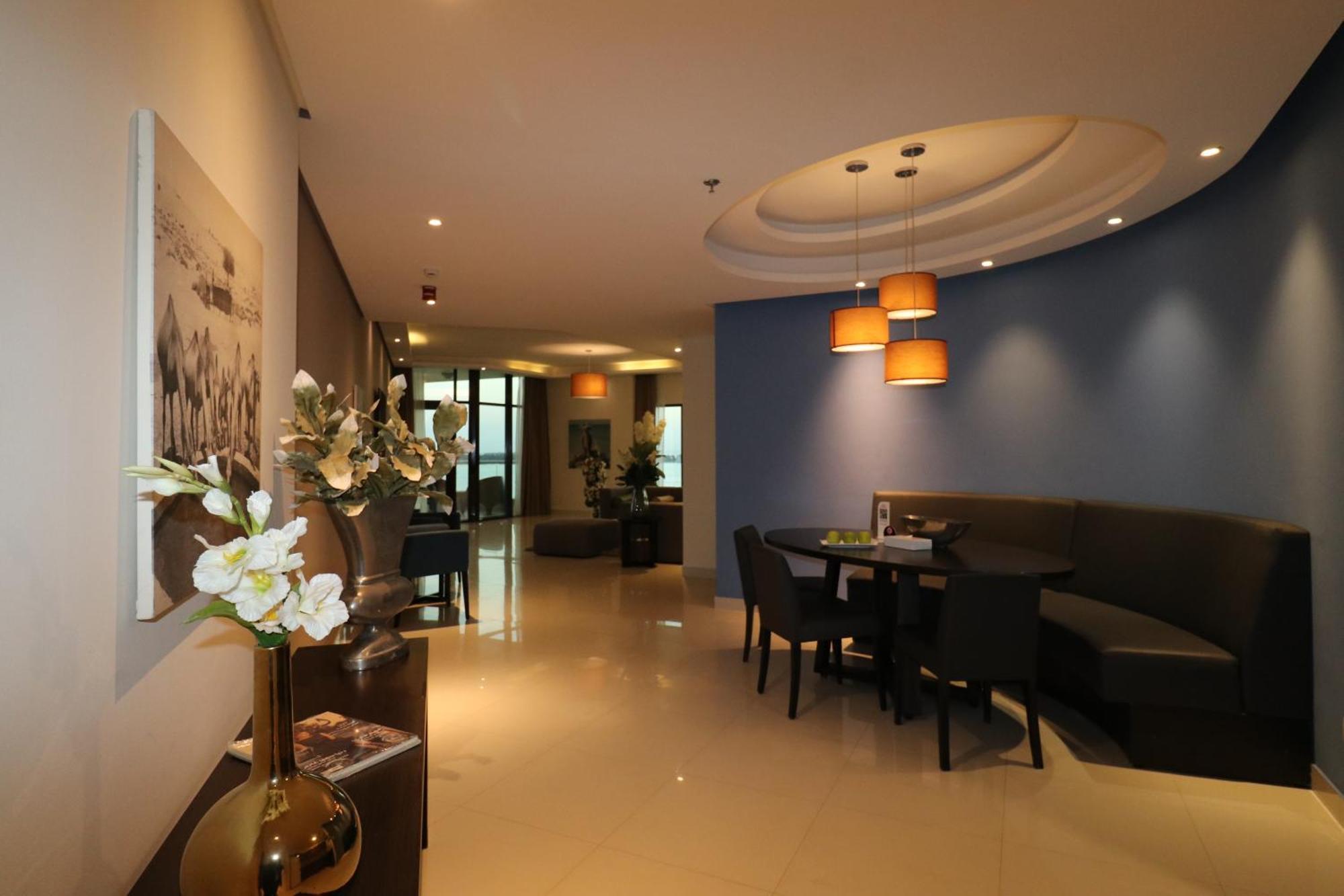 Lagoona Beach Luxury Resort And Spa Manama Eksteriør billede The photo showcases an interior space, likely a modern lounge or reception area. It features a combination of soft lighting, neutral-colored walls, and decorative elements. There are elegant light fixtures hanging from the ceiling, and a curved blue 