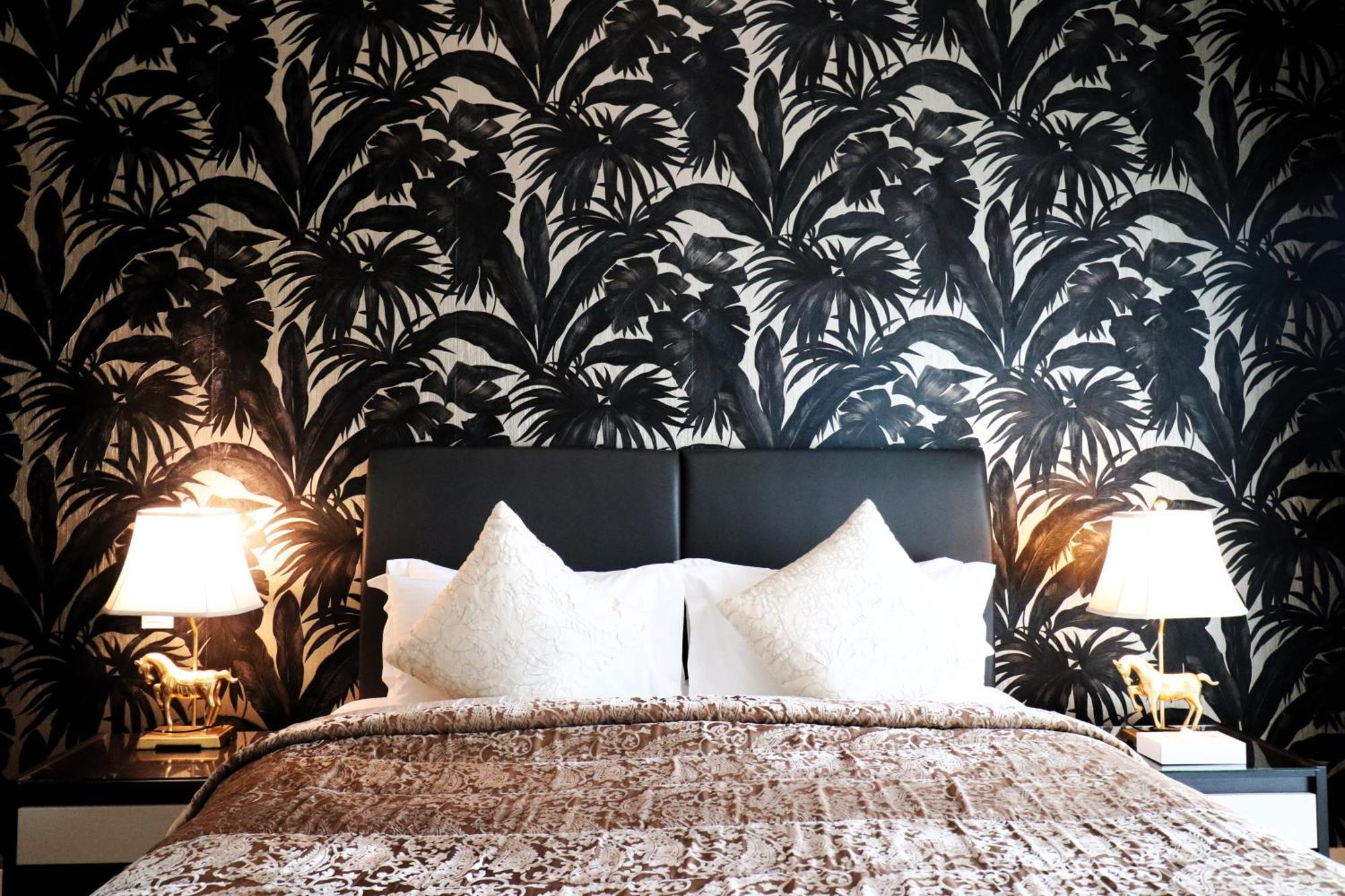Lagoona Beach Luxury Resort And Spa Manama Eksteriør billede The photo depicts a stylish bedroom featuring a distinctive wall covered in a black and white tropical foliage wallpaper. The bed has a modern black headboard and is adorned with white pillows, creating a clean and elegant look. A textured brown thro