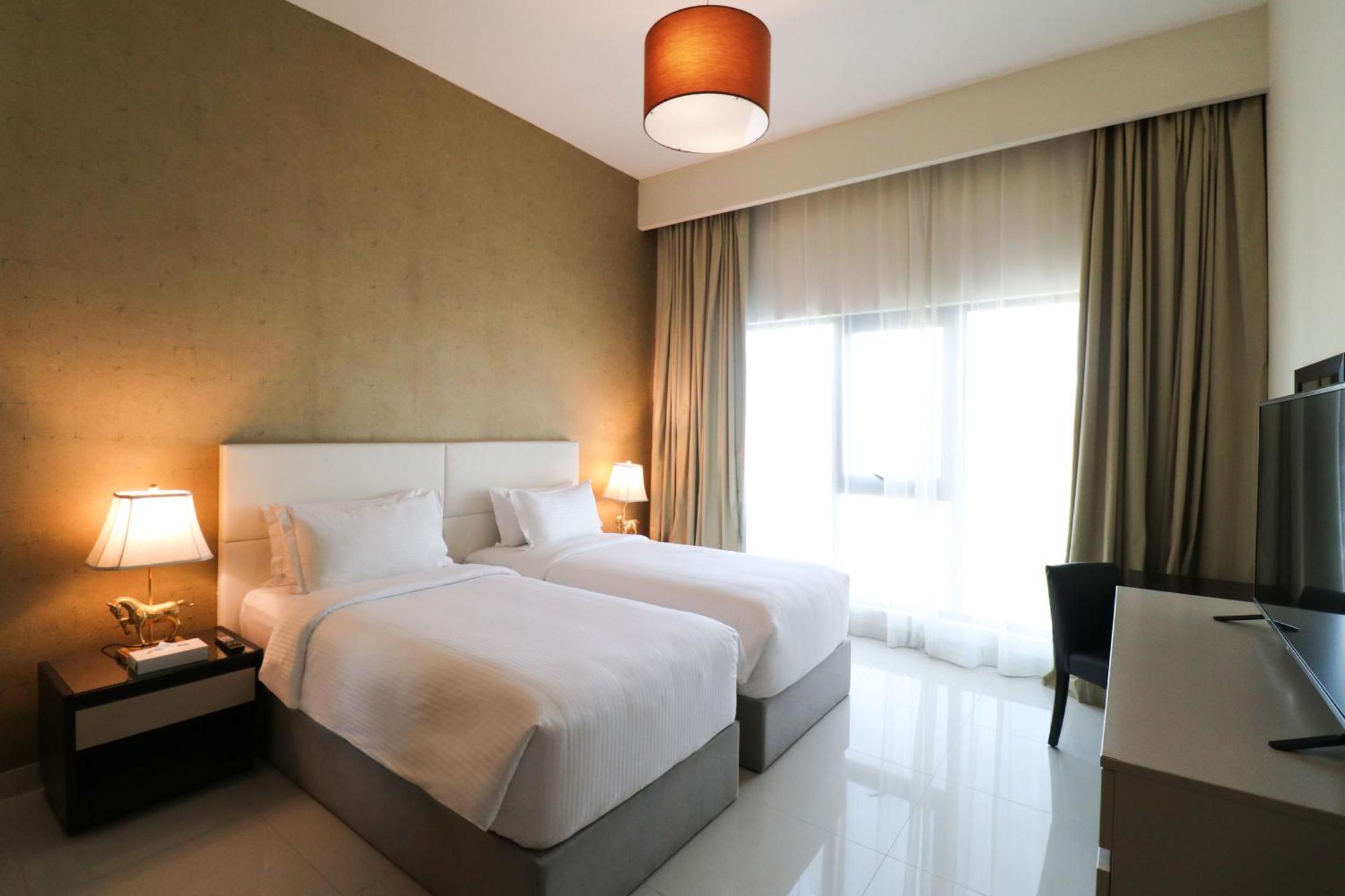 Lagoona Beach Luxury Resort And Spa Manama Eksteriør billede The photo shows a hotel room featuring two single beds with white bedding. The walls have a neutral tone, and there's a large window covered by light, sheer curtains allowing natural light to enter. On either side of the beds, there are bedside table